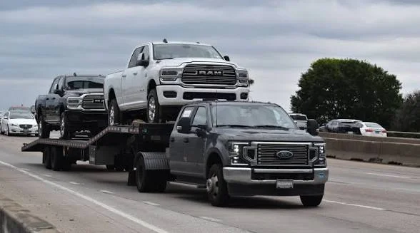 A flatbed tow truck hauling multiple pickup trucks on a highway.