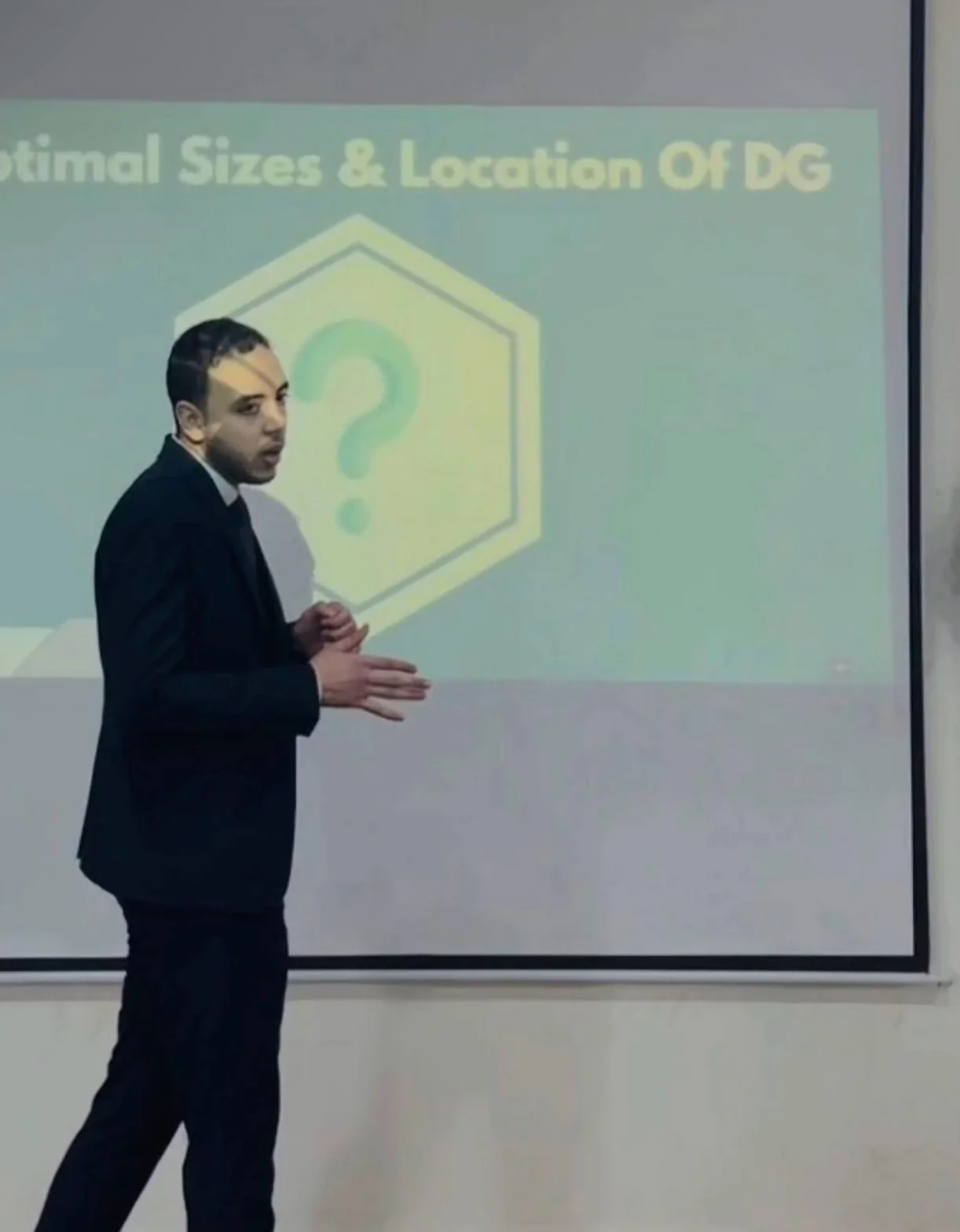 The tutor presenting at a conference, gesturing toward a projected slide.