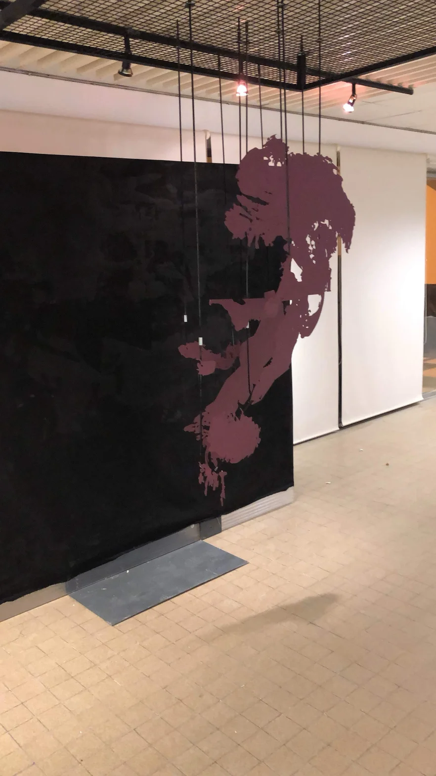 An industrial interior with dramatic black partition wall featuring large burgundy abstract silhouette suspended metal grid ceiling and spotlights