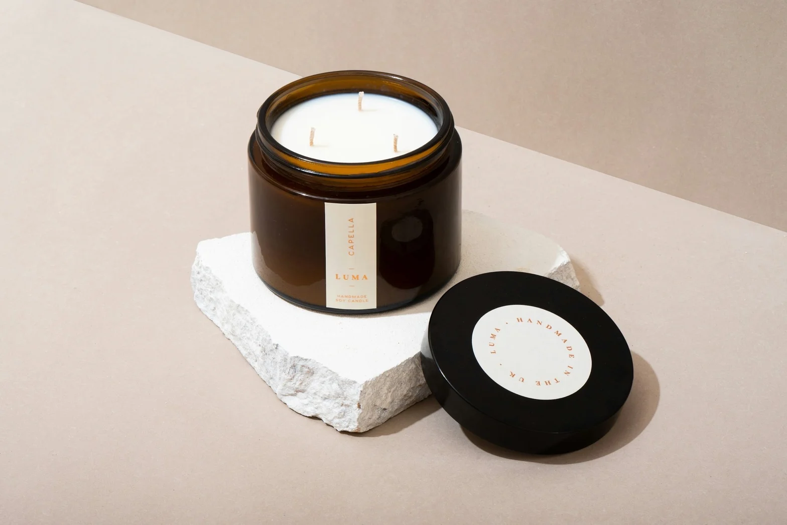 Open amber glass jar candle with three wicks styled beside its black lid