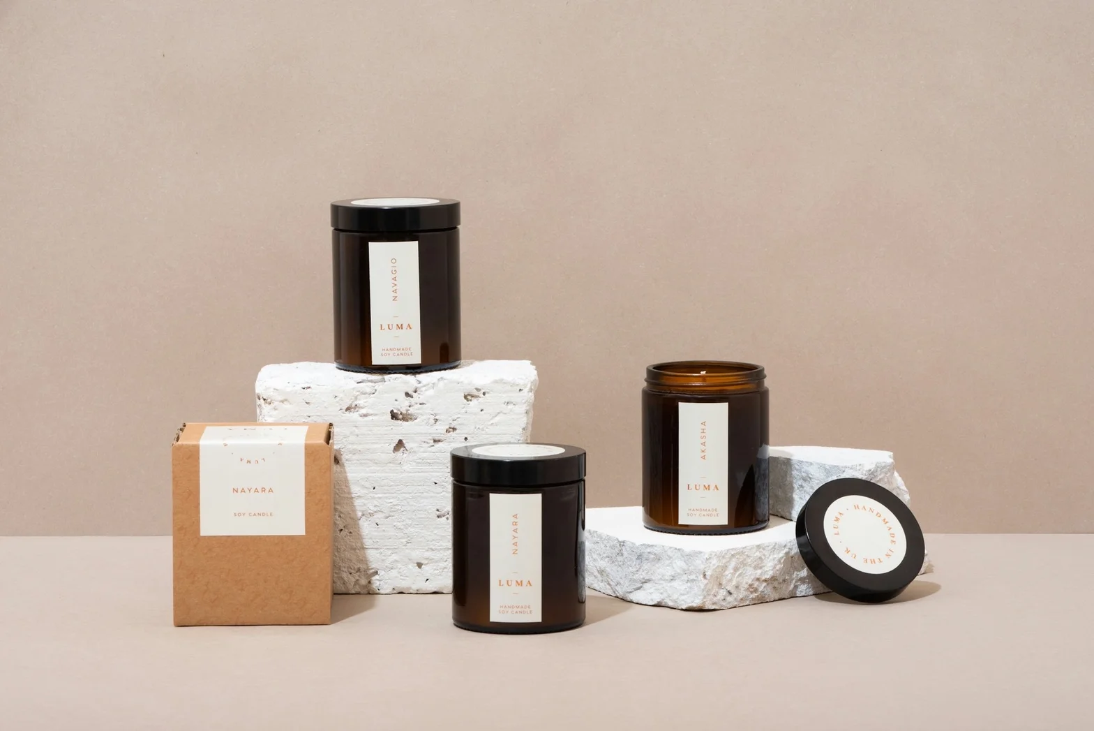 Handmade soy candles in dark glass jars and kraft gift box on white stone blocks