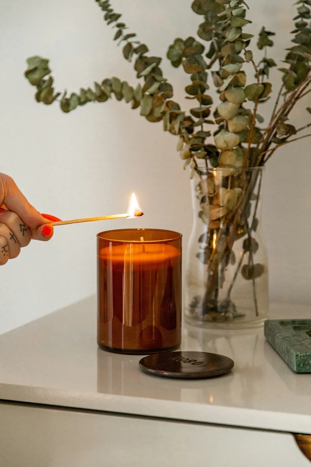 Lighting an amber glass candle with a match beside dried eucalyptus branches