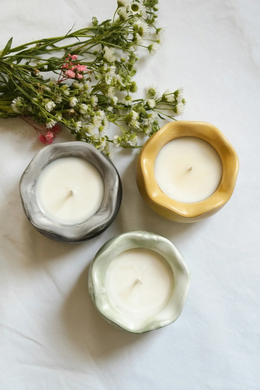 Three handmade ceramic candle vessels styled with delicate white and pink flowers