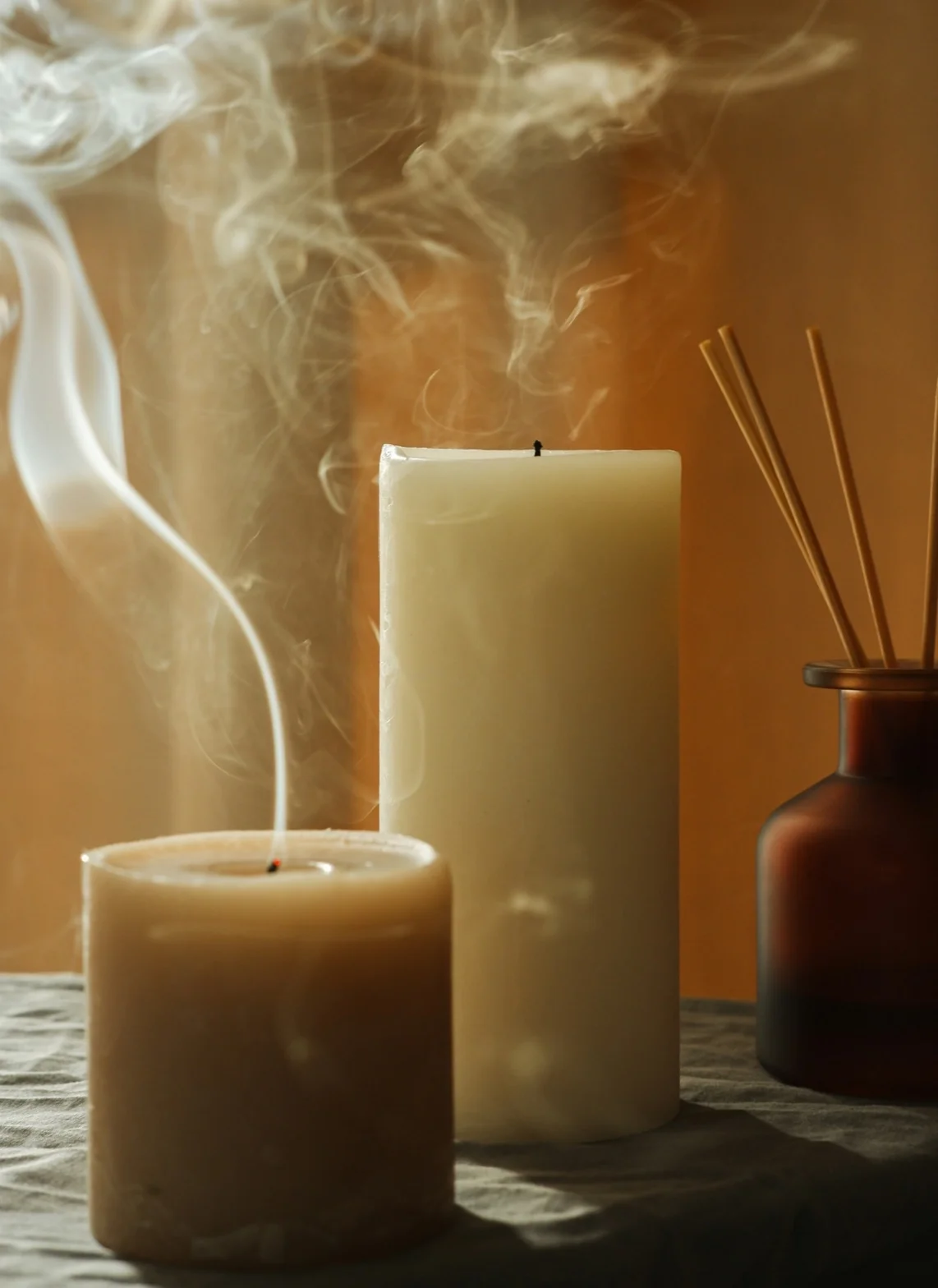 Cream pillar candles with drifting smoke and amber reed diffuser on a table
