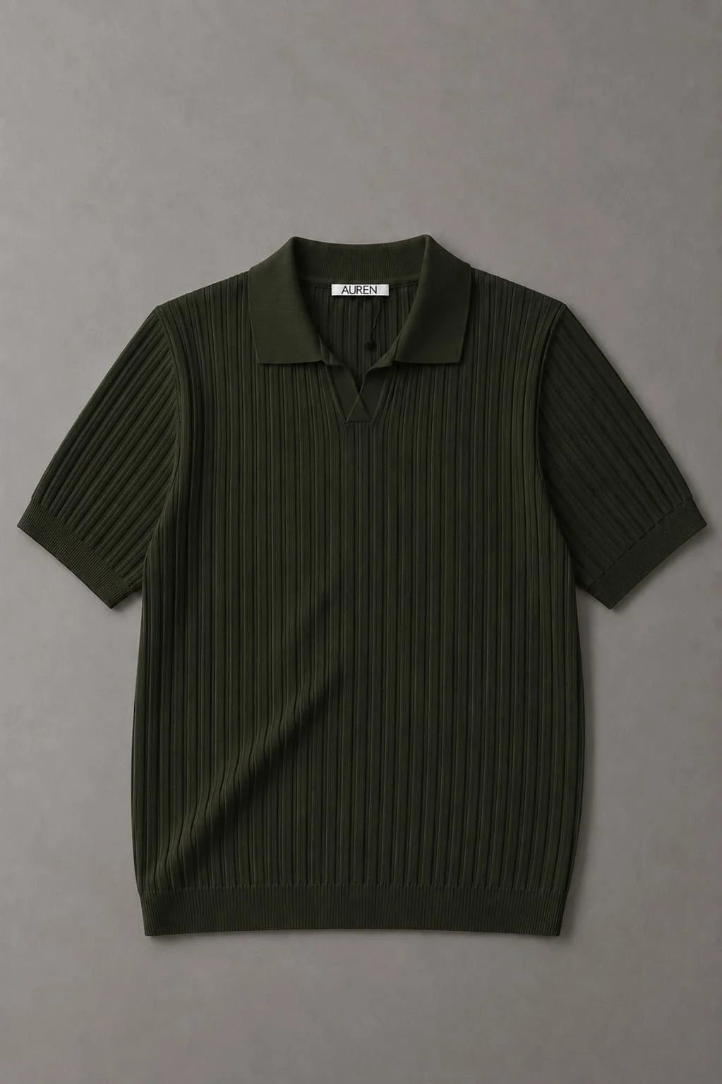 Camisa polo masculina verde-escura, com textura plissada vertical, gola clássica e mangas curtas, apresentada sobre um fundo cinza neutro.
