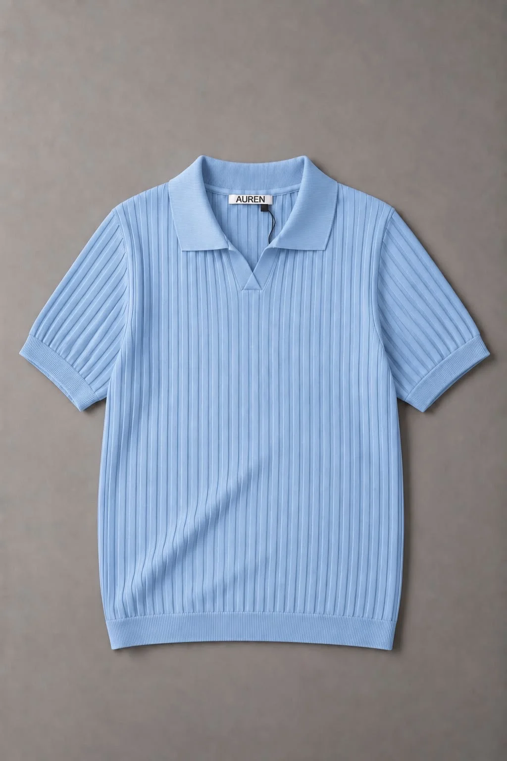 Camisa polo de malha azul-clara com textura canelada vertical, gola clássica e mangas curtas, fotografada sobre um fundo neutro.
