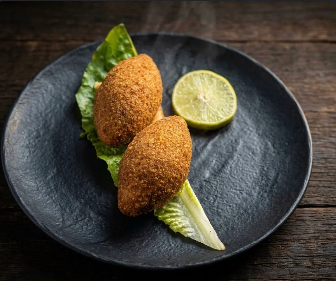 Two golden-brown crispy croquettes served on lettuce with a lime half on a dark plate.