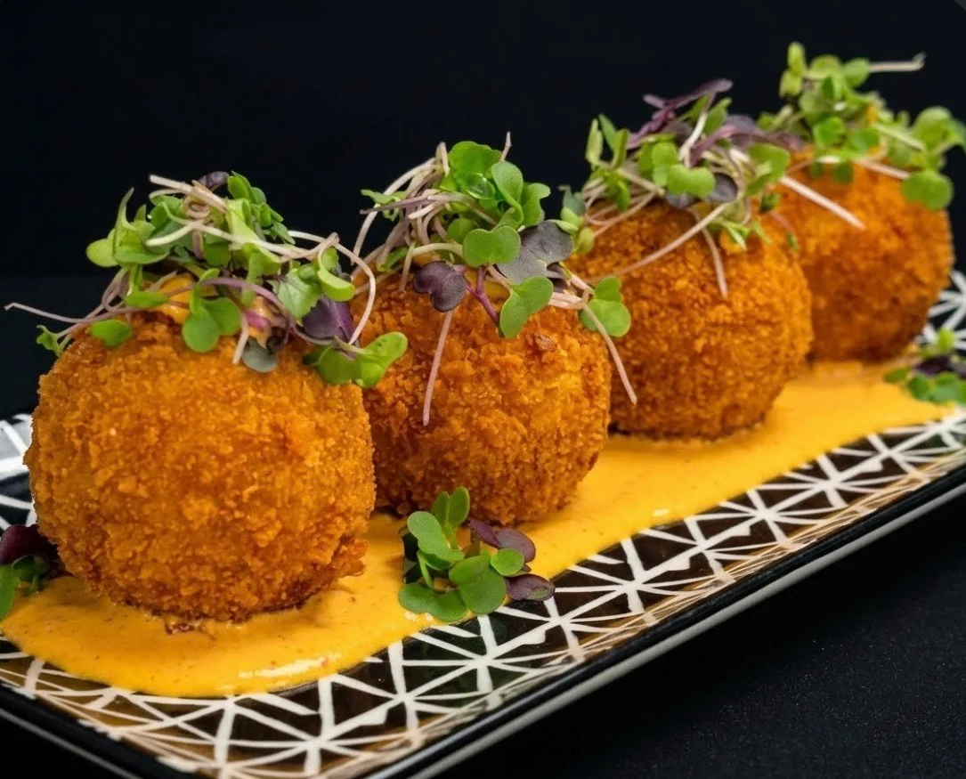 Golden-breaded croquettes topped with fresh microgreens and served with creamy yellow sauce.