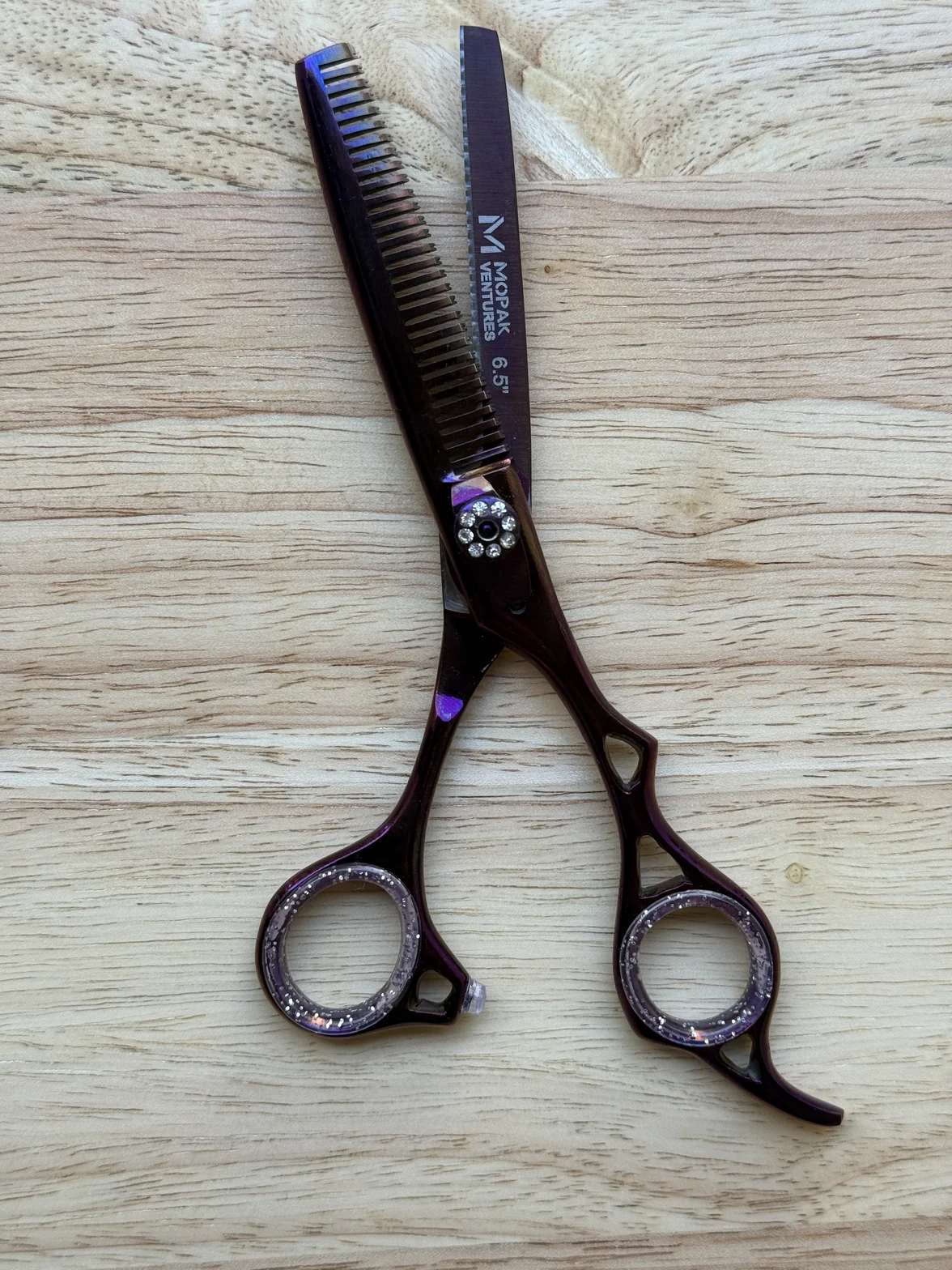 Professional hair-cutting scissors and thinning shears with dark purple handles on a light wood surface