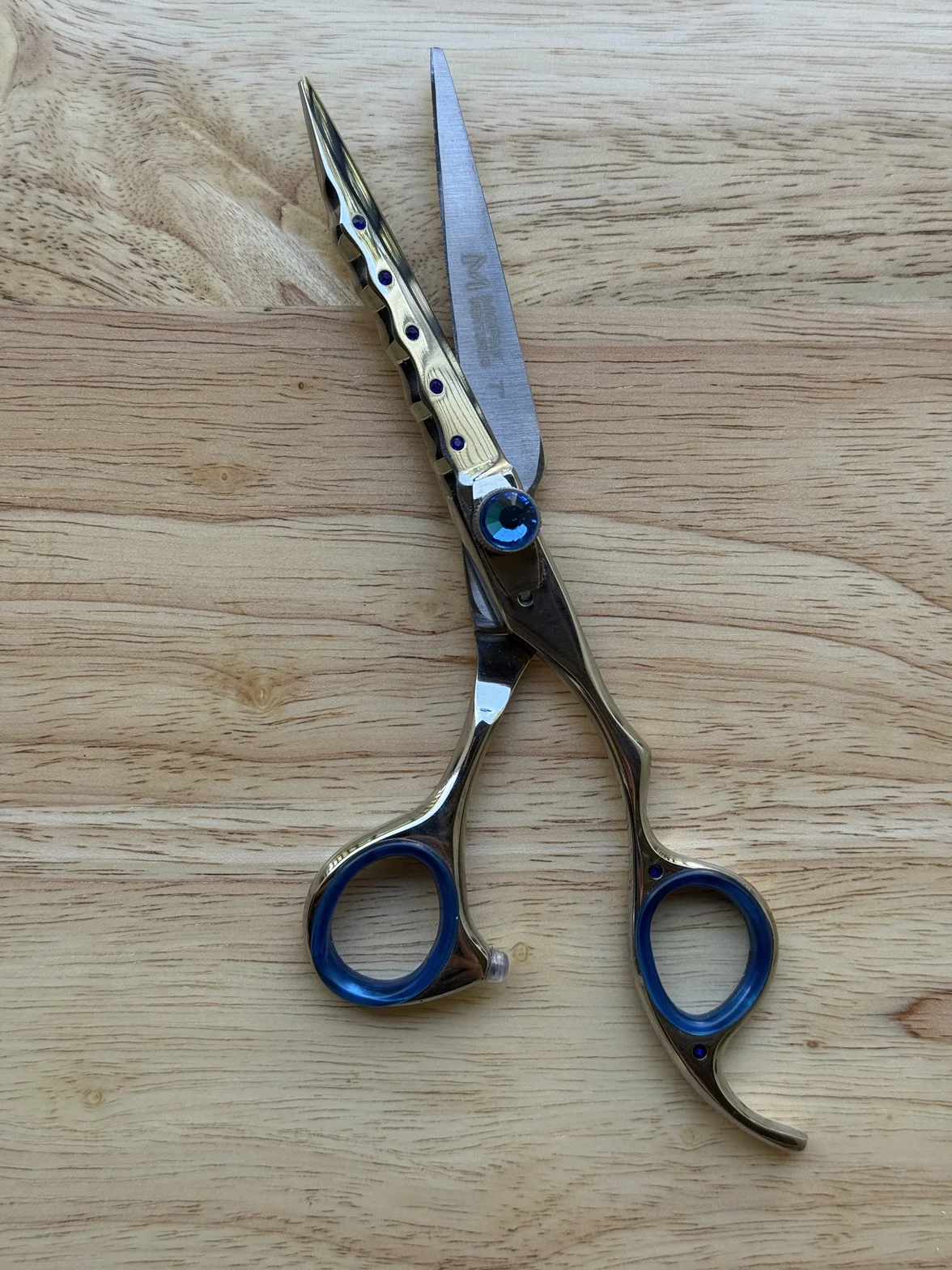 Professional hairdressing scissors with polished metal blades and blue finger rings on a light wood surface