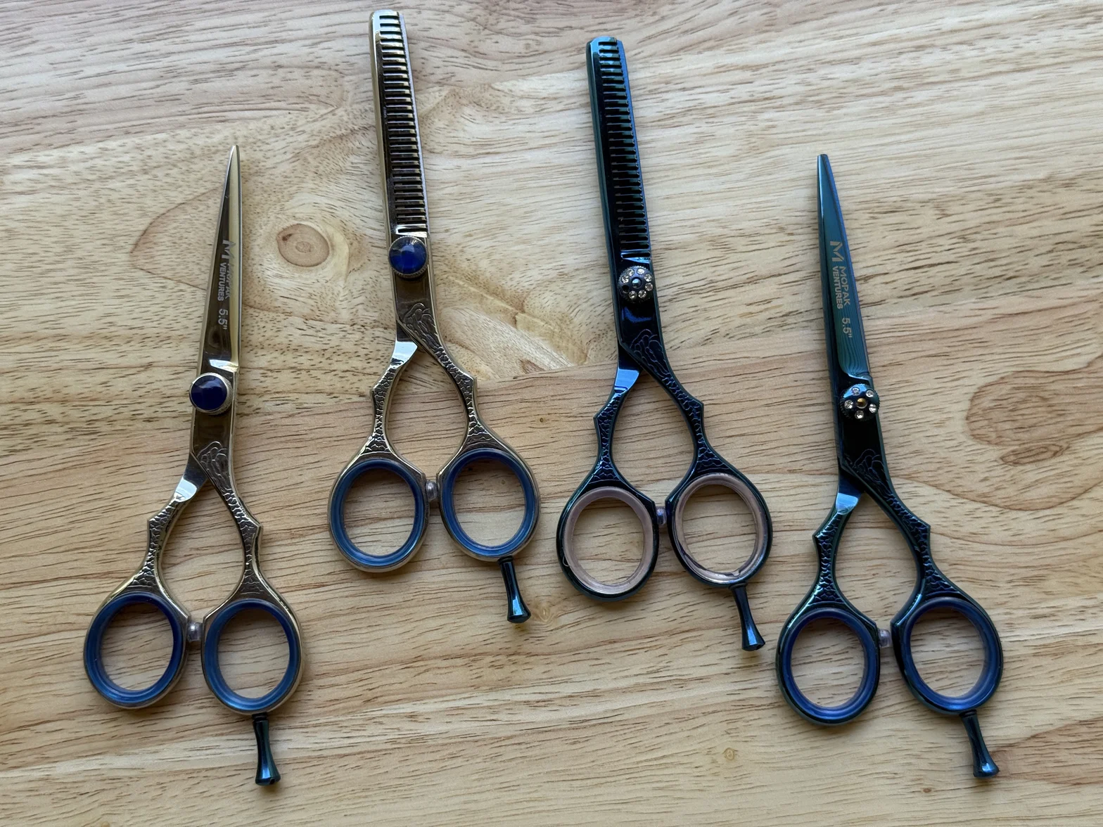 Three professional hairdressing scissors and texturizing shears with blue accents on a light wooden surface