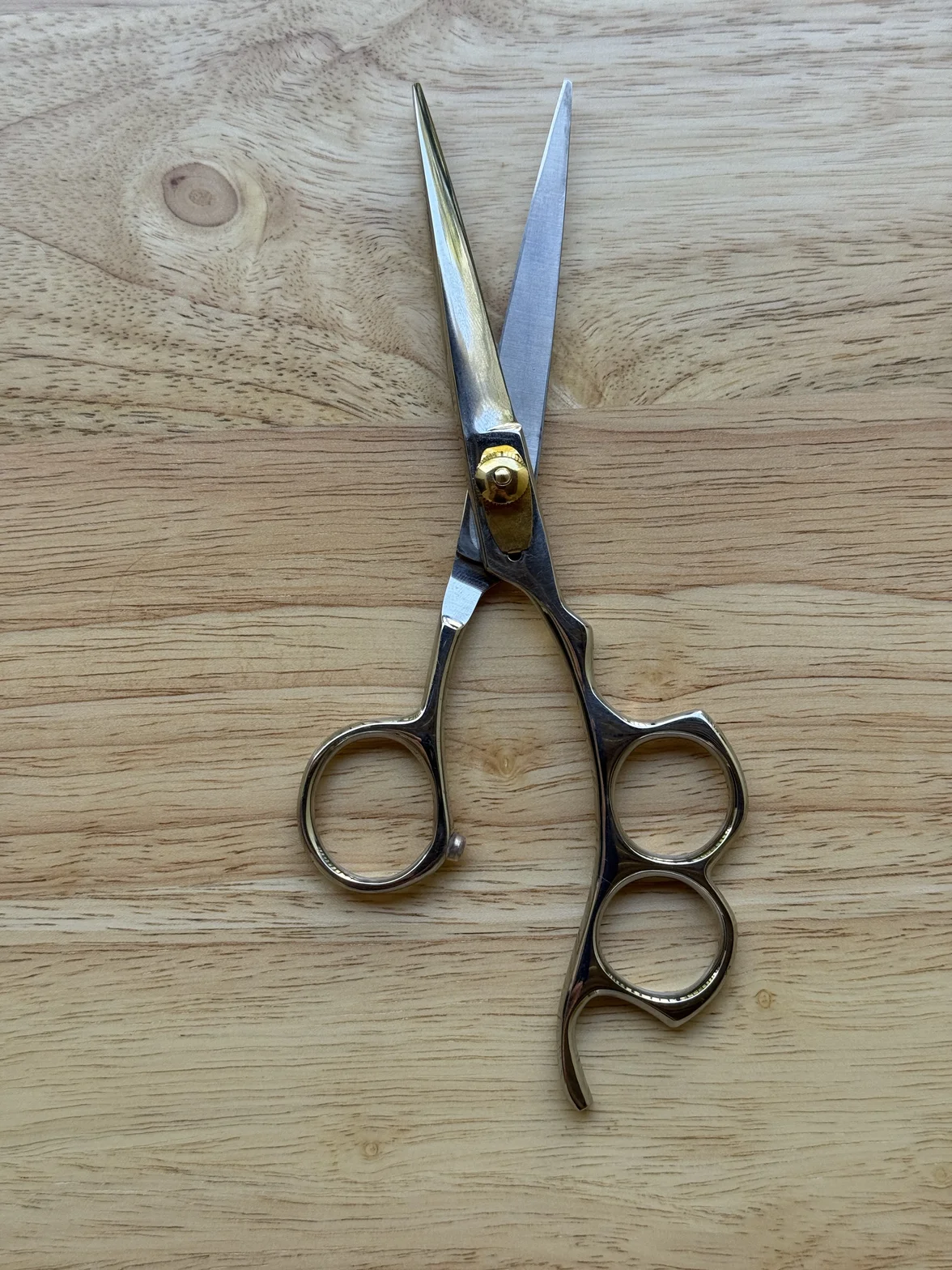 Polished professional hair-cutting scissors displayed open on a light wood surface