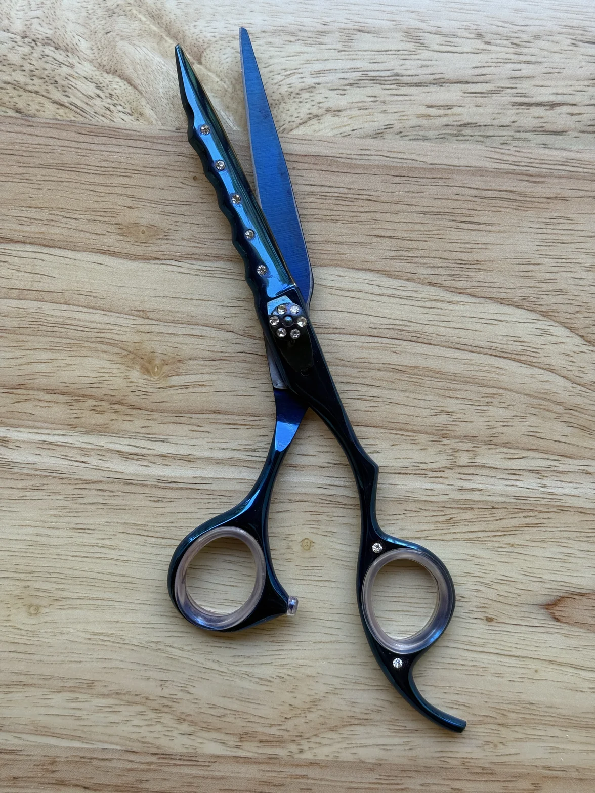 Blue-and-black professional hair-cutting scissors with decorative finger rings on a light wood surface