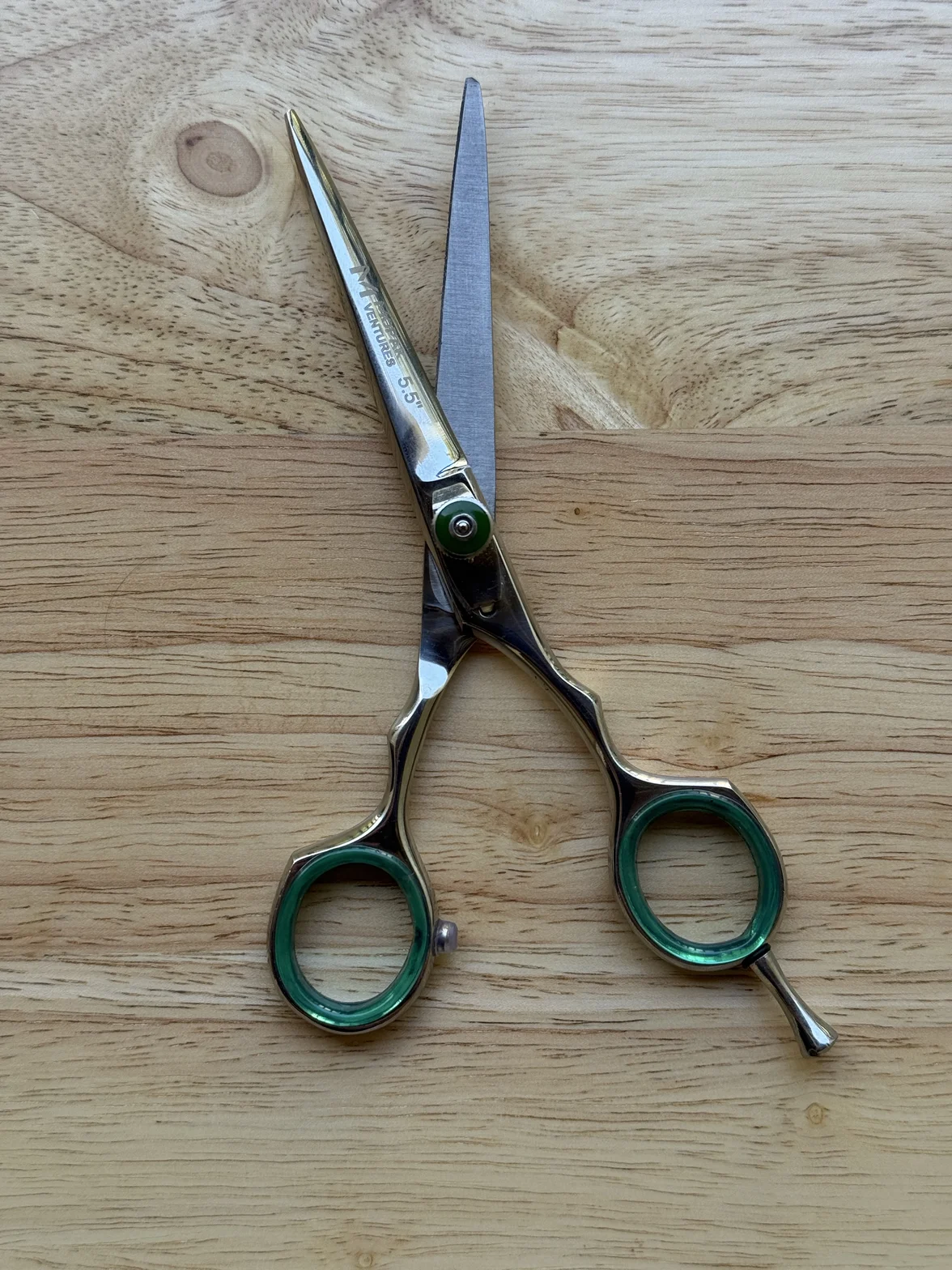 Polished professional hair-cutting scissors with emerald-green finger rings on a light wooden surface