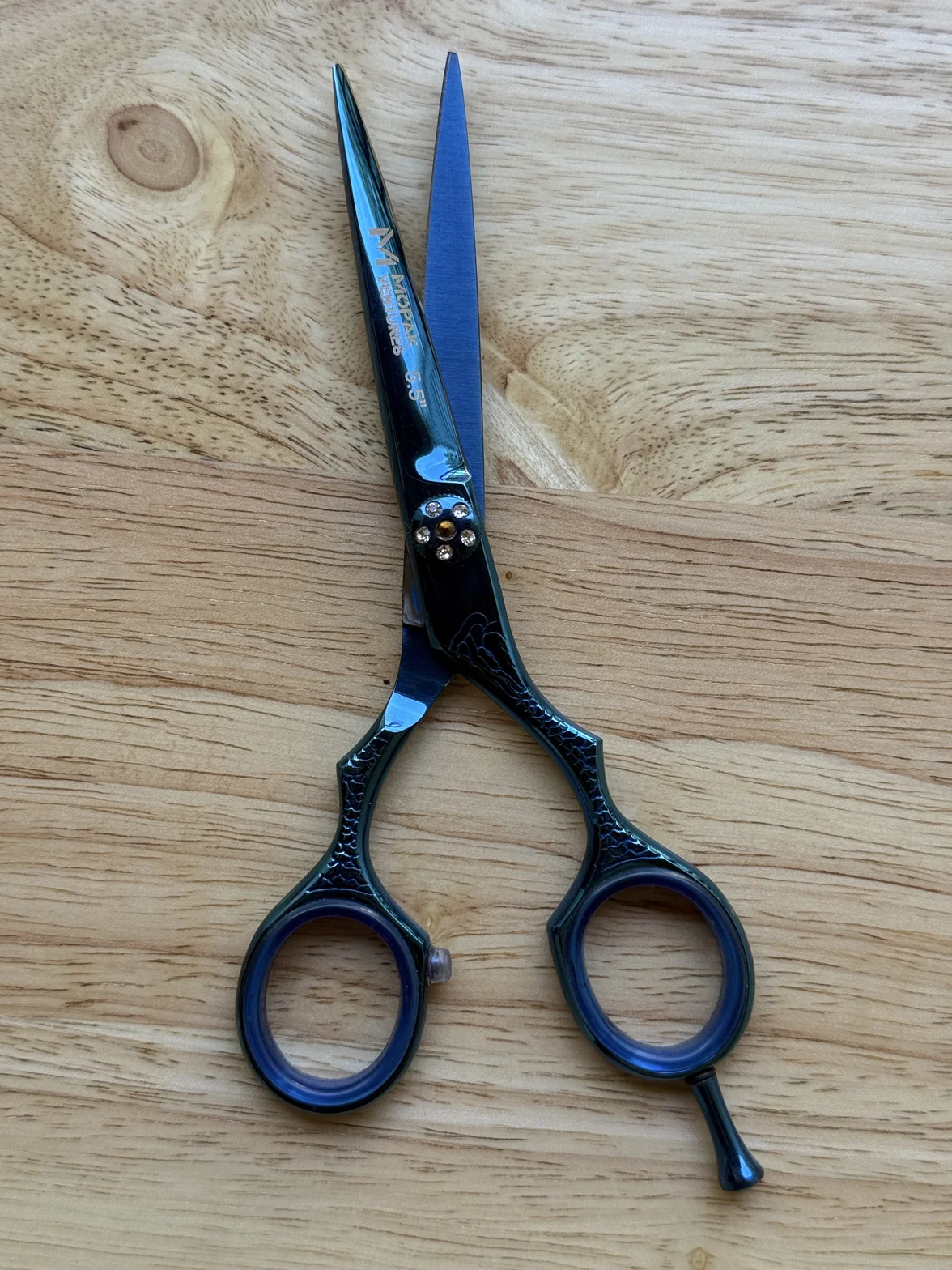 Professional hair-cutting scissors with dark blue and black textured handles on a light wooden surface