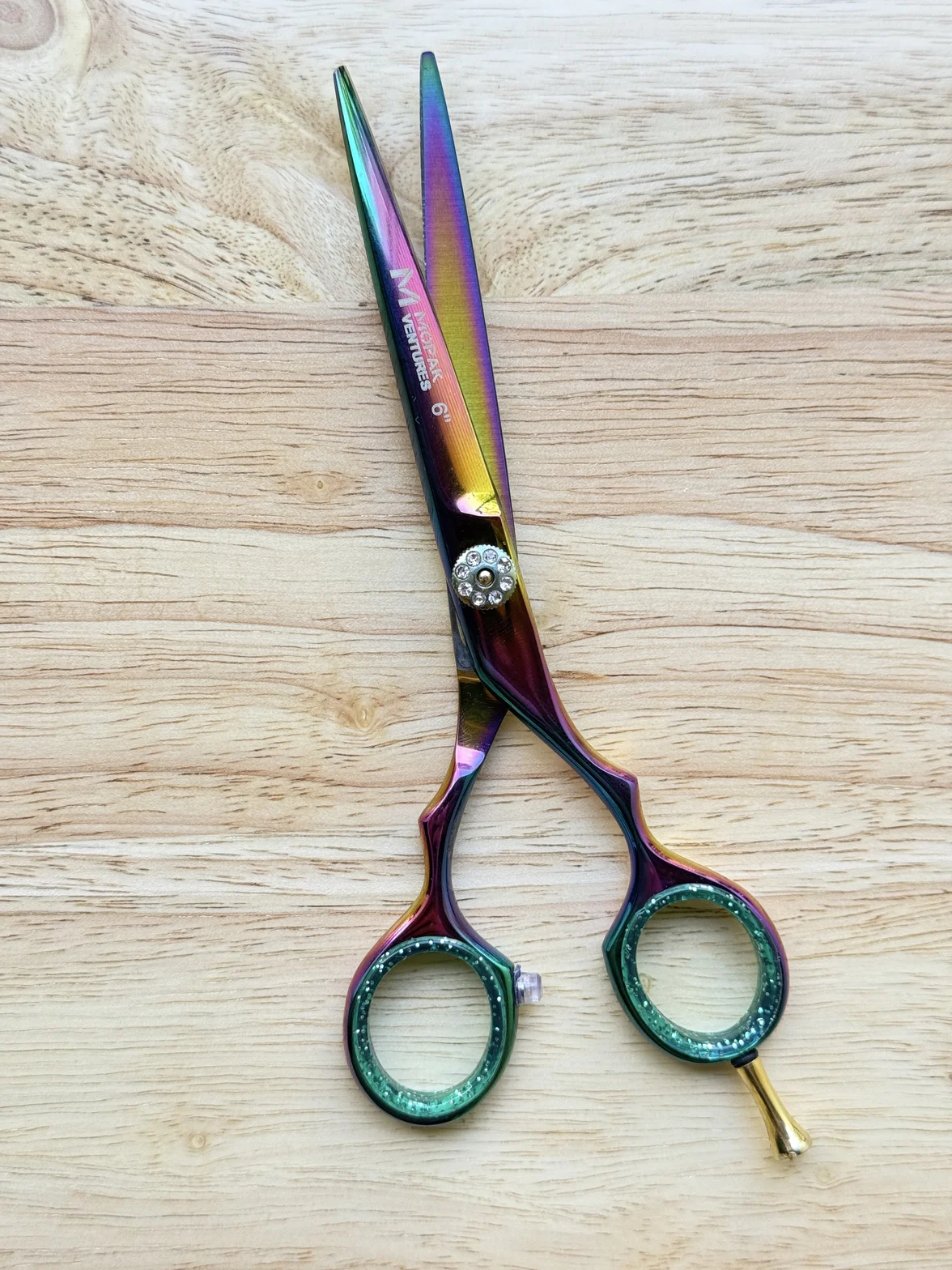 Ornate iridescent hair-cutting scissors with jeweled finger rings on a light wood surface