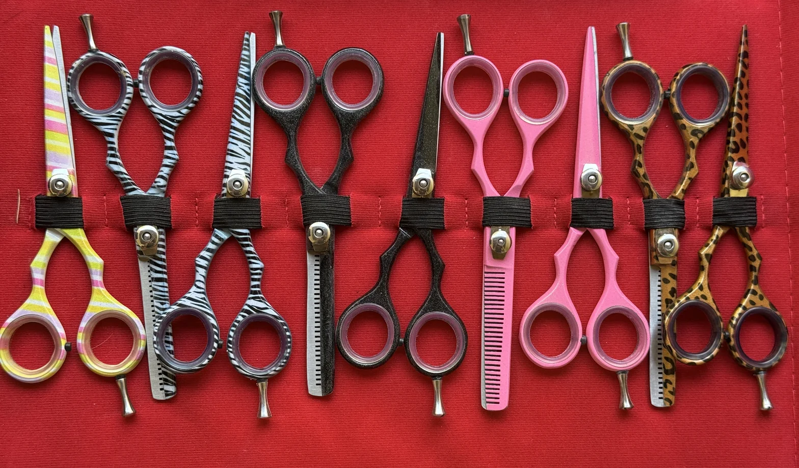 Neatly arranged collection of colorful professional hair-cutting and thinning scissors on a red fabric background