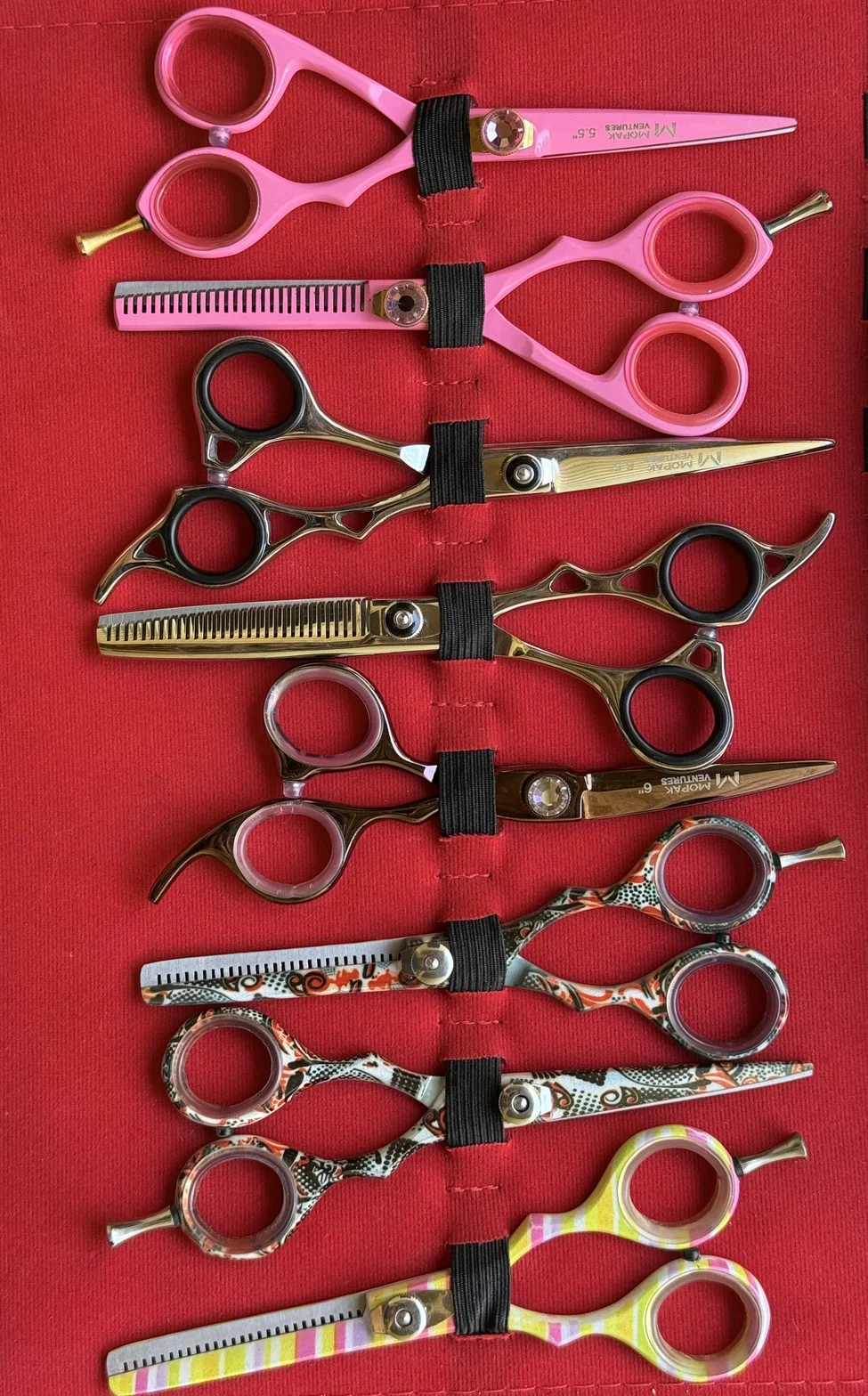 Professional hair-cutting scissors and thinning shears in assorted finishes on a red fabric roll