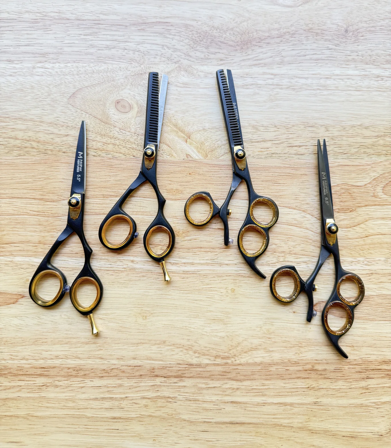 Professional hairdressing scissors and texturizing shears arranged on a light wooden tabletop