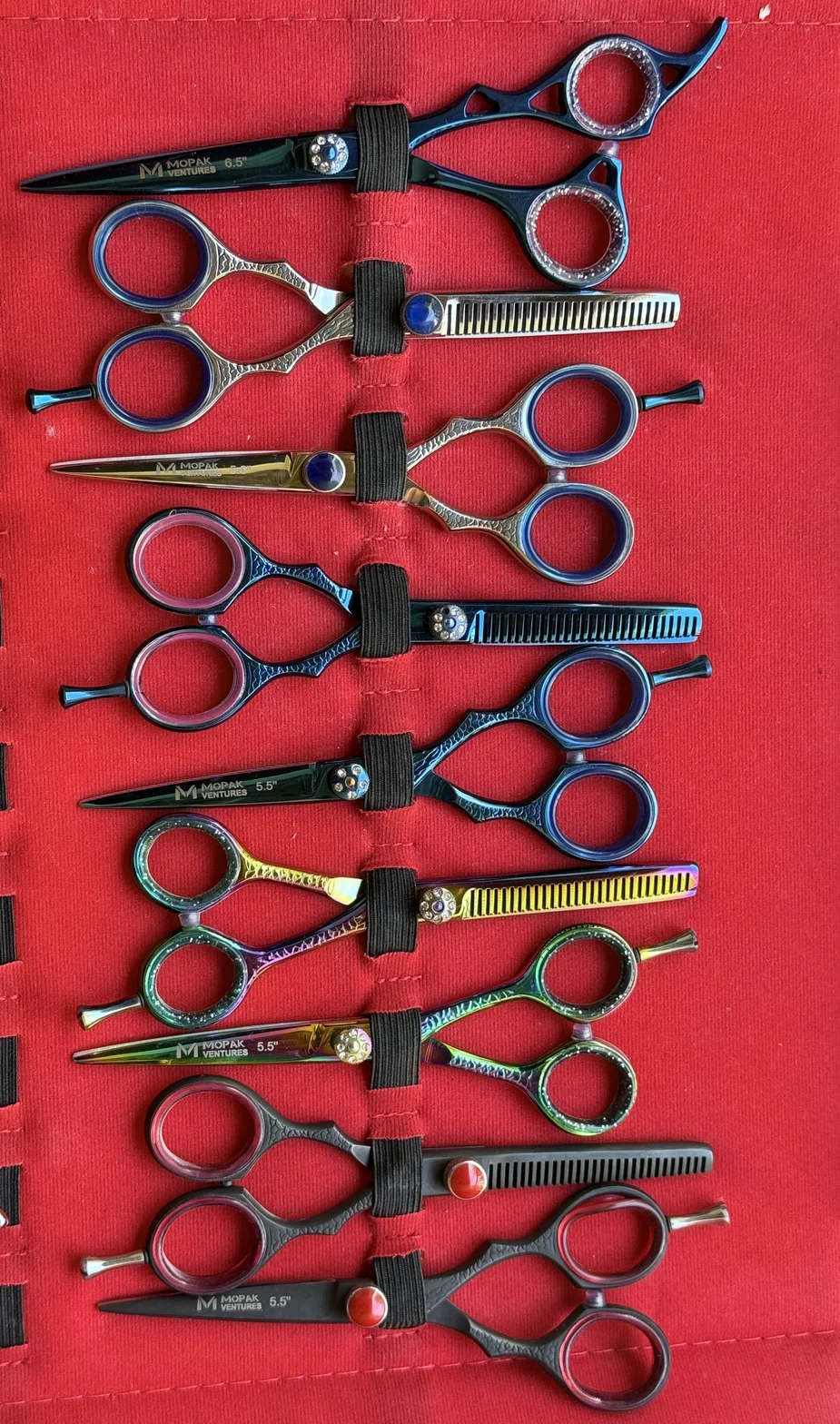 Colorful professional hair-cutting scissors and thinning shears arranged vertically on a red fabric display