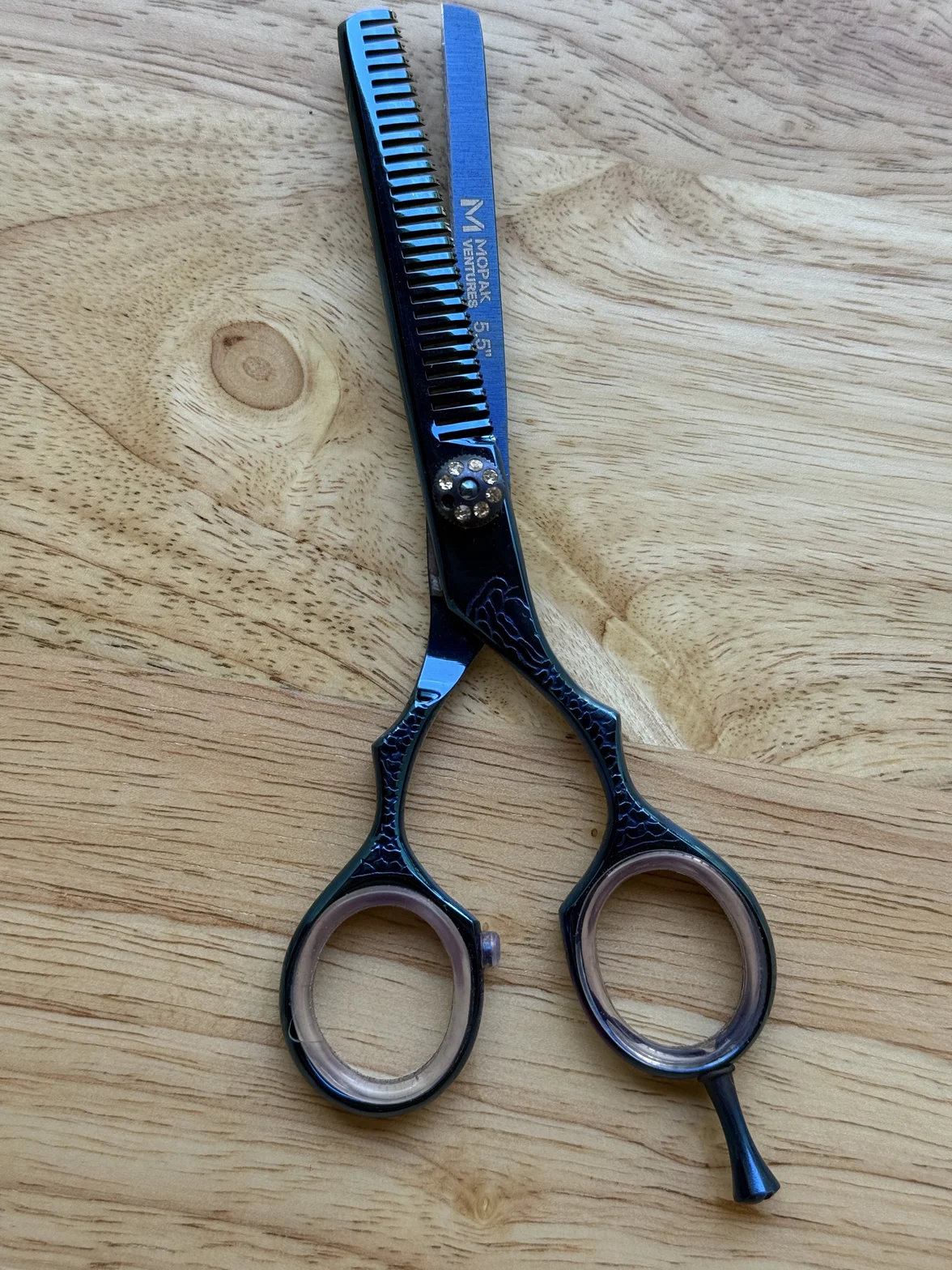 Black and blue professional hair-cutting thinning shears with decorative handles on a light wood surface