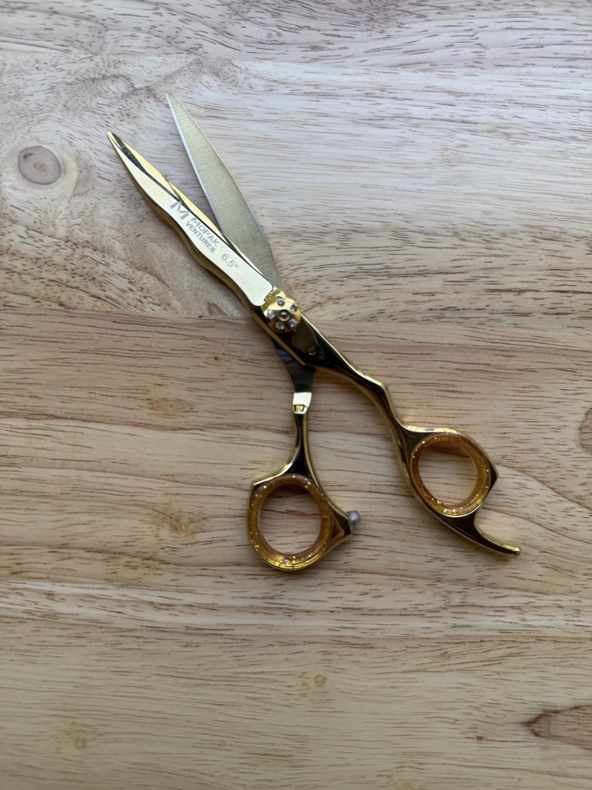 Polished gold-toned professional hairdressing scissors resting on a light wooden surface