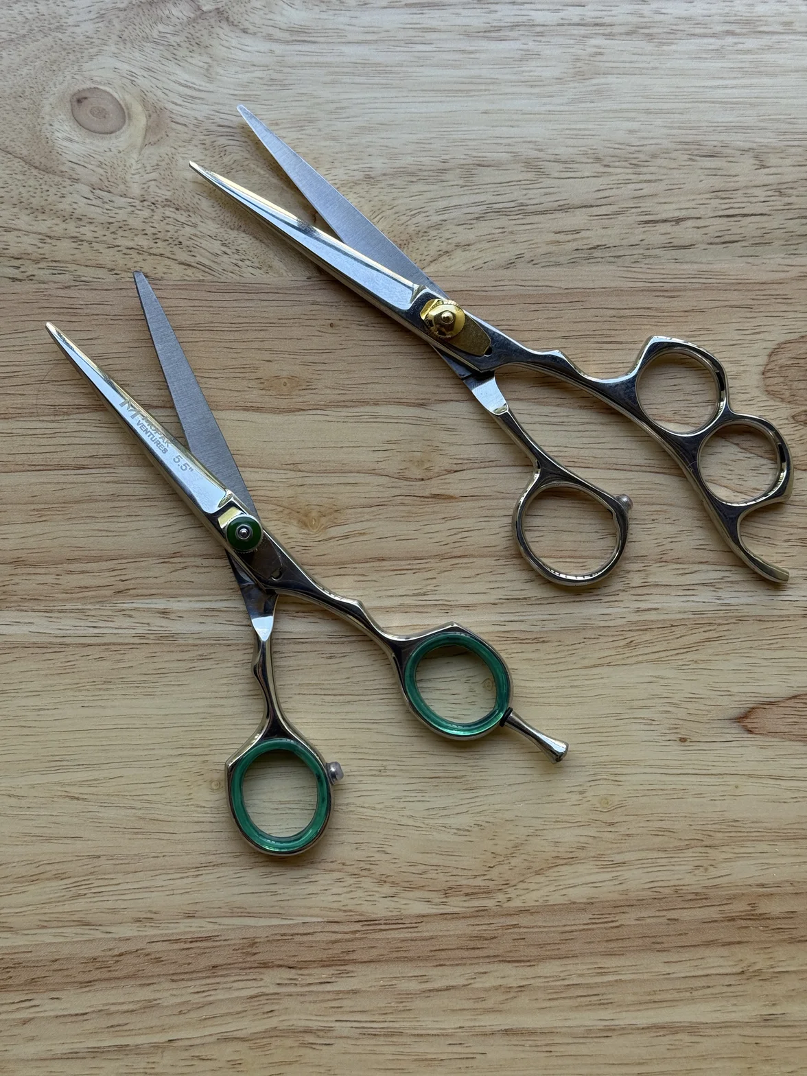 Two professional hairdressing scissors, including a thinning shear and a cutting shear, arranged on a light wooden surface