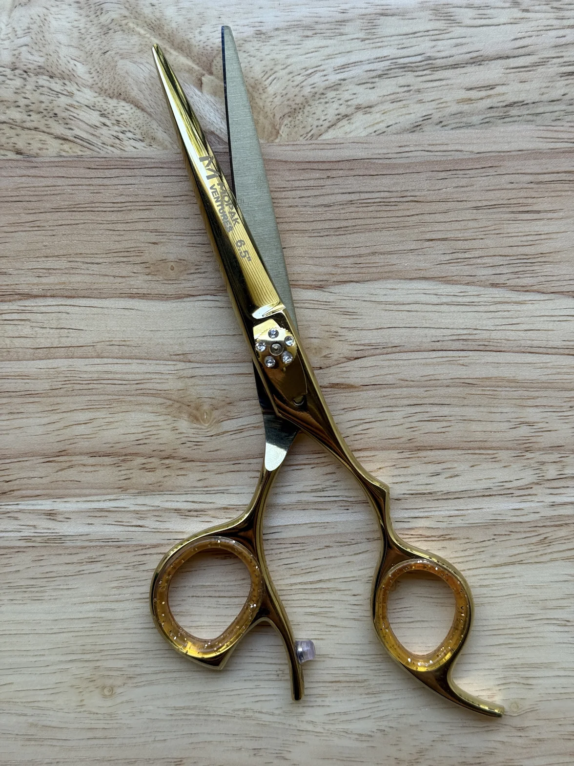 Gold-colored professional hair-cutting scissors with engraved branding on a light wood surface