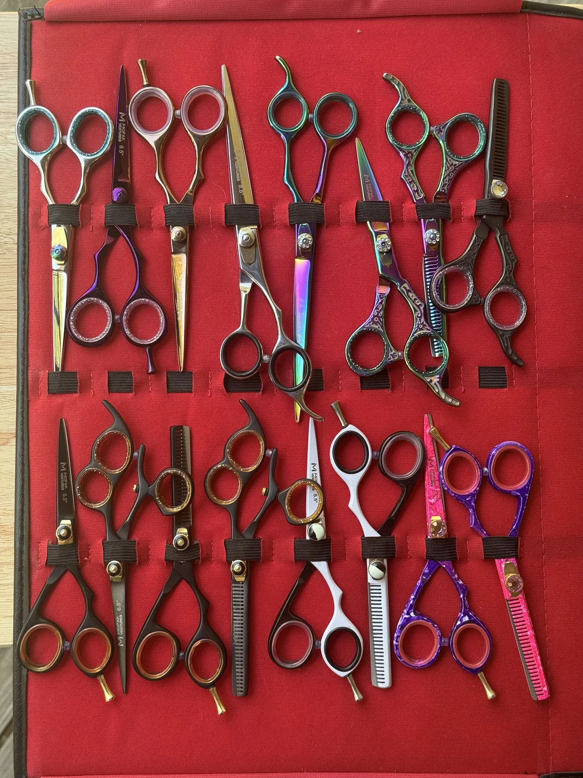 Professional hair-cutting and texturizing scissors, combs, and shears arranged in holders on a red display case