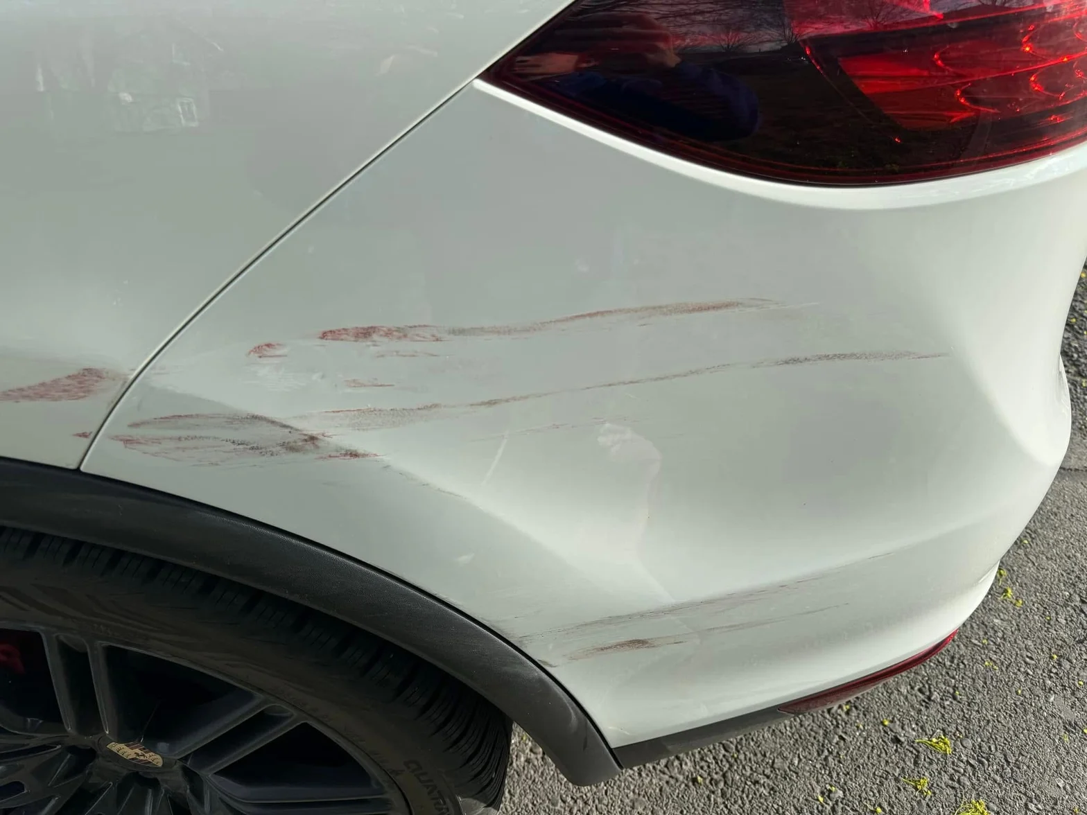 Close-up of a white vehicle rear side panel showing scratches and surface scuffs before detailing