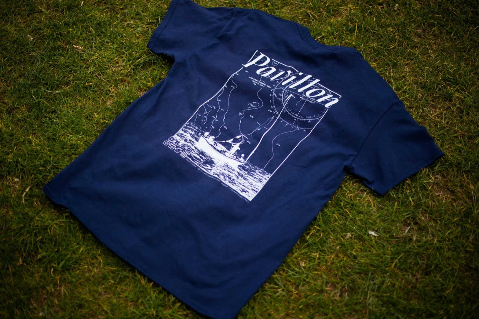 Navy blue graphic T-shirt laid flat on grass with map illustration