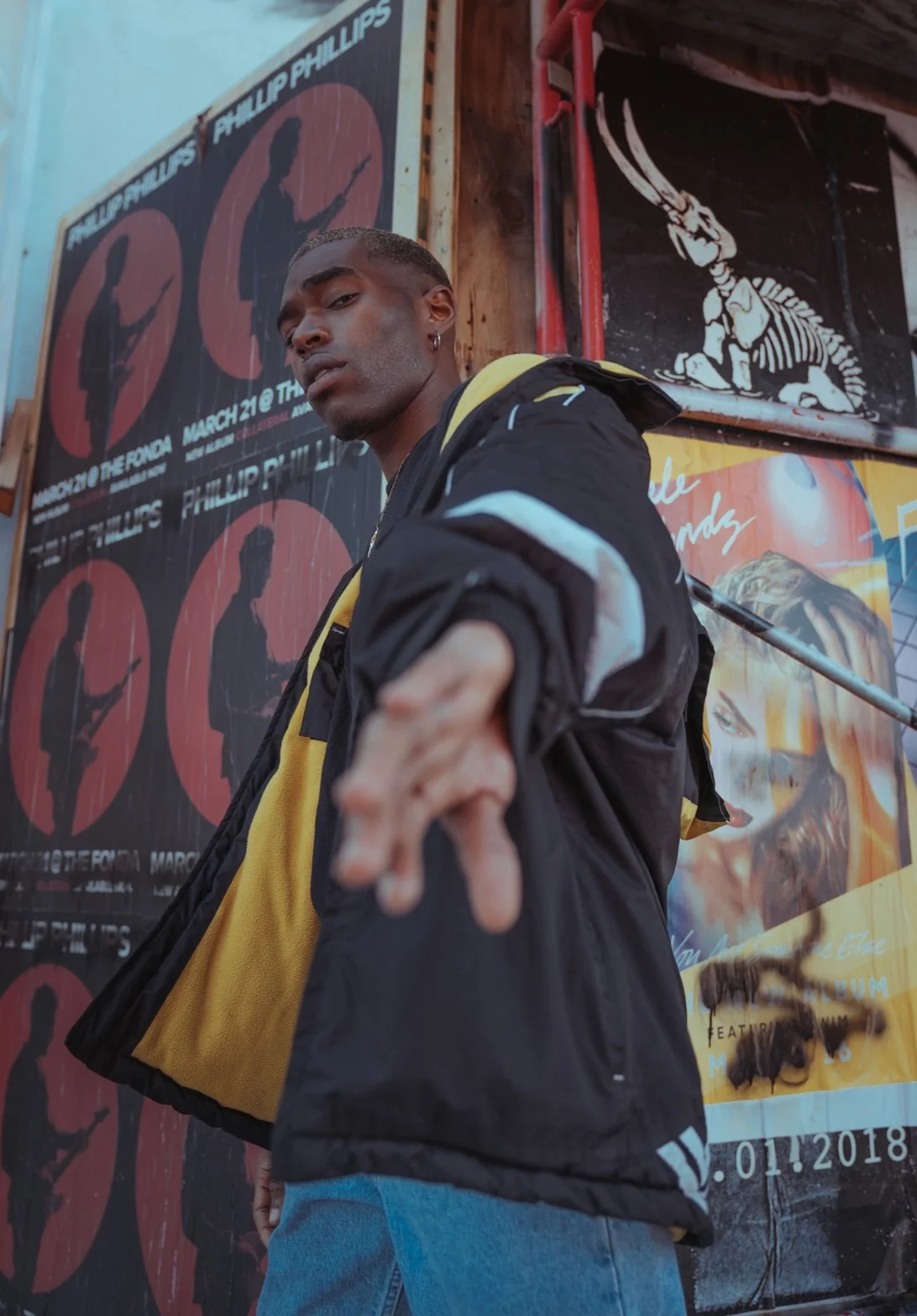 Portrait of model wearing black and yellow streetwear jacket in front of poster wall
