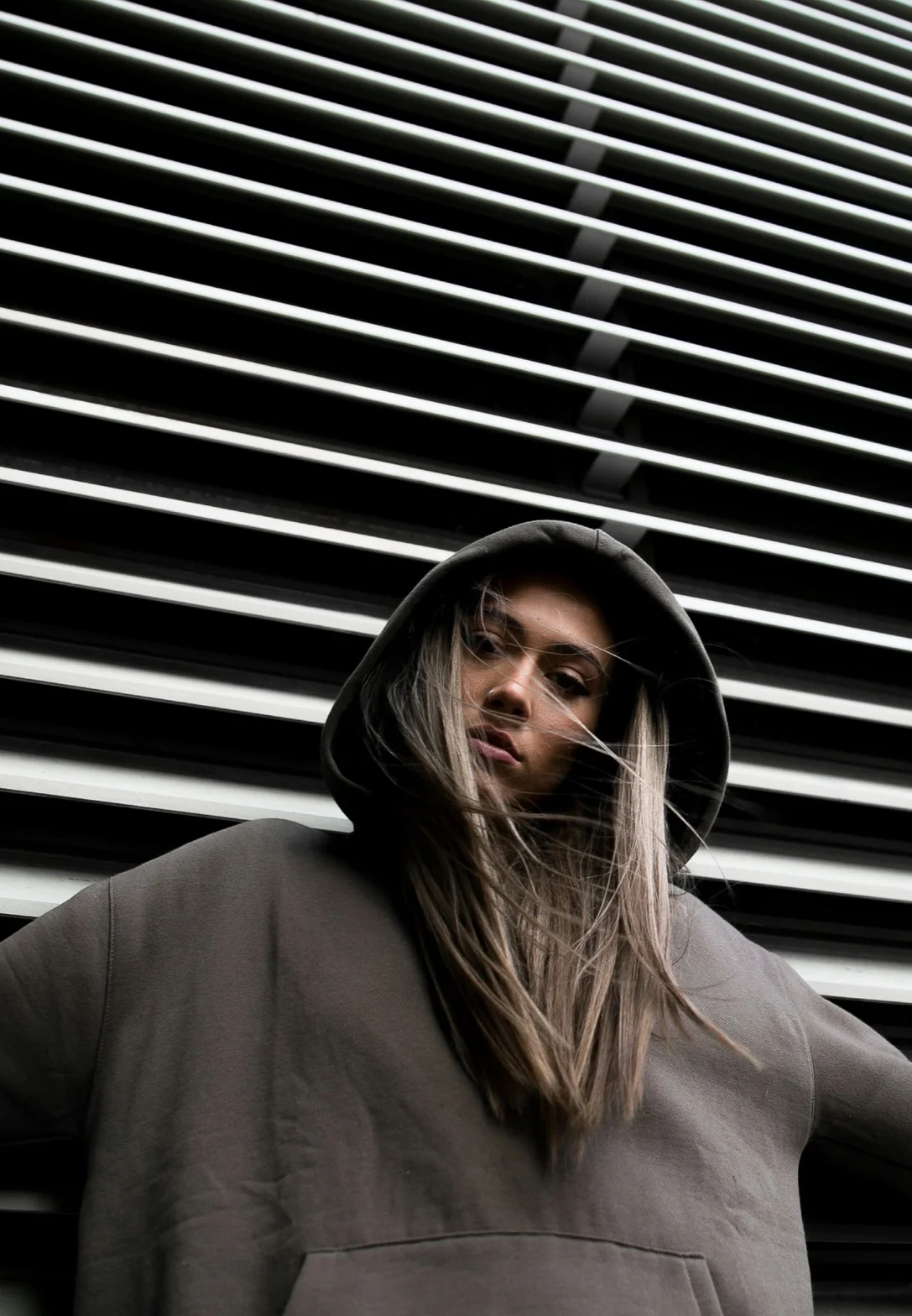 Editorial portrait of a model wearing a heavyweight black hoodie against striped architectural backdrop