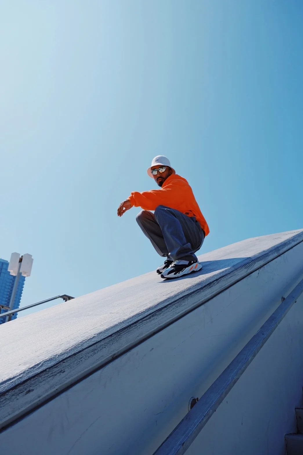 Model crouching on urban rooftop wearing streetwear and bucket hat